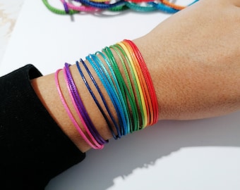 May include: A rainbow colored string bracelet with multiple strands of different colors, including red, orange, yellow, green, blue, indigo, and violet.