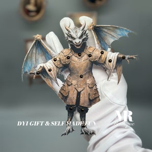 May include: A papercraft dragon puppet with wings, wearing armor and holding a sword. The dragon is brown, gray, and white. The puppet is on a white gloved hand. The text "DIY GIFT & SELF MADE FUN" is below the puppet.