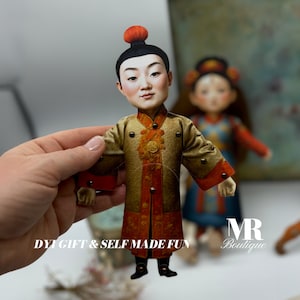 May include: A paper doll of a person wearing a gold and red robe with a red hat. The doll is holding its arms out to the sides. The doll is standing on a white surface. DIY GIFT & SELF MADE FUN is written on the surface.