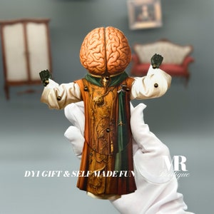 May include: A papercraft puppet with a brain for a head, wearing a gold and green robe. The puppet is holding its arms out and has a DIY gift & self-made fun text on the bottom.