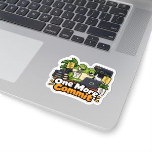 Puede incluir: Una pegatina troquelada que muestra una rana verde trabajando en un portátil con el texto One More Commit. La rana sostiene una taza con la etiqueta Fueled By, rodeada de libros con el texto Code Coffee Repeat, una planta y notas adhesivas.