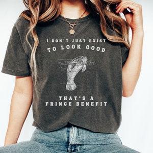 May include: A dark gray t-shirt with a white graphic of a manatee and the text "I don't just exist to look good. That's a fringe benefit."