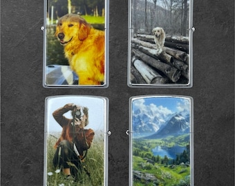 May include: Four silver lighters with different images. One shows a golden retriever dog near water. Another depicts a dog on logs in a forest. A third shows a person taking a photo in a field. The last one has a landscape of mountains and a lake.