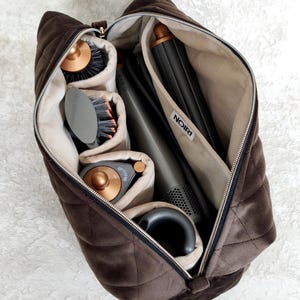 May include: A dark brown quilted velvet storage bag with a zipper closure, containing a hair styling tool set. The interior features beige lining, multiple compartments, and a white label with the text NOIRI. The set includes various attachments.