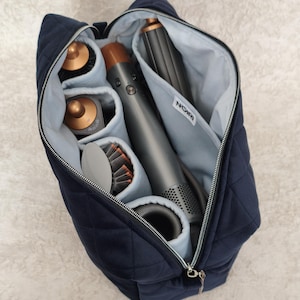 May include: A navy blue quilted storage bag with a light blue interior lining, featuring multiple internal compartments organized to hold a hair styling tool and various attachments. A white label with the text NOIRI is sewn inside the bag.