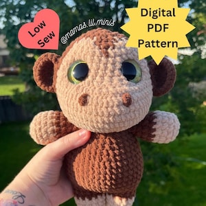 May include: A crocheted monkey amigurumi toy with brown and beige fur, large green eyes, and a stitched nose. The toy is being held by a hand. The image includes the text "Low Sew" and "@mamas.lil.minis" in a heart shape and "Digital PDF Pattern" in a star shape.