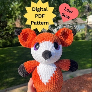 Puede incluir: Un juguete de peluche de zorro tejido a crochet con pelaje naranja, blanco y negro. El juguete tiene grandes ojos morados y una nariz negra. El juguete está siendo sostenido por una mano con un tatuaje. La imagen incluye el texto "Digital PDF Pattern" y "Low Sew".
