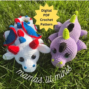 May include: Two crocheted dragon plushies, one white with red and blue accents, and one purple with green accents. The plushies are sitting on a bed of green grass. The text "Digital PDF Crochet Pattern" is on a yellow starburst. The text "mamas lil minis" is on the grass below the plushies.