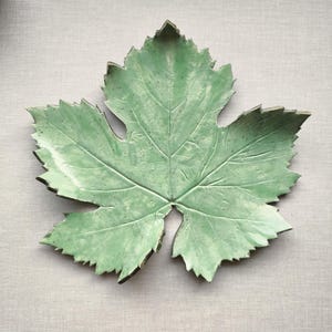 Pode incluir: Um prato de servir de cerâmica verde em forma de folha. O prato é detalhado com veias e uma superfície texturizada.