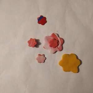 May include: Five colorful clay flower shapes on a white background. The flowers are in shades of pink, red, blue, and yellow.
