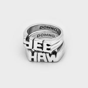 Peut inclure: Deux bagues en argent empilées l'une sur l'autre. La bague du haut porte le mot "YEE" et la bague du bas porte le mot "HAW". Les deux bagues portent l'inscription "DOMNO." à l'intérieur.
