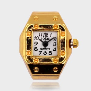 Peut inclure: Une montre-bague dorée avec un cadran carré blanc. Le cadran affiche des chiffres et des aiguilles noirs, avec le mot "QUARTZ" en dessous du centre. La bague a une forme rectangulaire avec une petite couronne sur le côté.