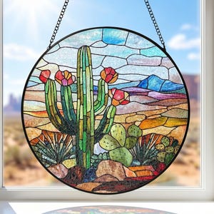 May include: A circular stained glass window panel depicting a desert cactus scene. The panel has a black metal frame and a chain for hanging. The cactus is green with red flowers, set against a colourful desert landscape.