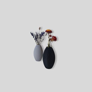 May include: Two ceramic vases with a ribbed texture. The vase on the left is light gray and holds dried lavender. The vase on the right is dark gray and holds dried flowers.