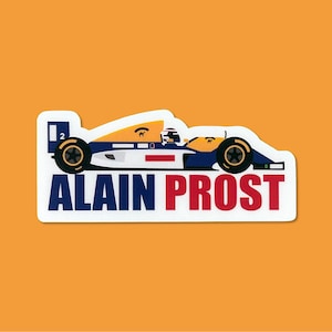 May include: A white, blue and yellow race car sticker with the text "ALAIN PROST" in red letters. The car has the number "2" on the side.
