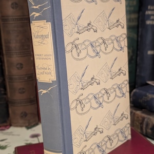 Könnte beinhalten: Ein blaues Hardcover-Buch mit dem Titel "Kidnapped" von Robert Louis Stevenson. Der Buchumschlag zeigt ein sich wiederholendes Muster aus einer Feder, einem Stück Papier und einem Seil.