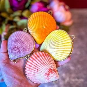 May include: Four seashells with gold trim, each painted in a different color: orange, purple, yellow, and pink.