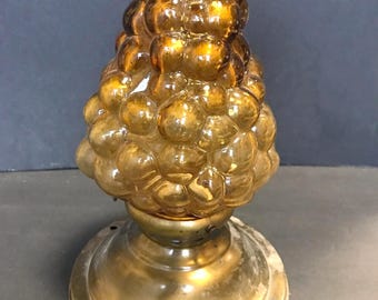 May include: A lamp featuring a textured, amber-colored glass shade shaped like a cluster of grapes, mounted on a circular, weathered brass base. The glass surface consists of numerous rounded, bubble-like protrusions that catch the light.