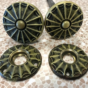 May include: Four antique brass door knobs and backplates. The knobs are round with a central button and a sunburst design. The backplates are circular with a matching design and a central hole for the door handle. The brass has a dark, aged patina.