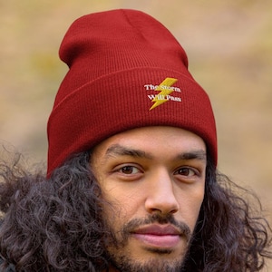 May include: A person wearing a red beanie with the text "The storm will pass" and a yellow lightning bolt graphic. The beanie is made of a soft, knitted fabric.