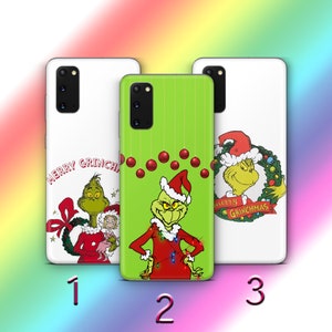 May include: Three phone cases featuring the Grinch from the popular Christmas movie "How the Grinch Stole Christmas". The first case is white with the text "Merry Grinchmas" and a green Grinch wearing a red Santa hat. The second case is green with a Grinch wearing a red Santa hat and holding Christmas lights. The third case is white with the text "Merry Grinchmas" and a green Grinch wearing a red Santa hat and holding a wreath.
