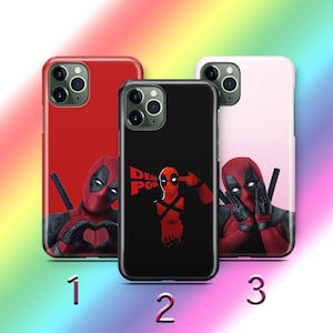 Puede incluir: Tres fundas de teléfono diferentes con Deadpool. La primera funda es roja con Deadpool haciendo un corazón con las manos. La segunda funda es negra con Deadpool apuntándose una pistola a la cabeza. La tercera funda es rosa con Deadpool cubriéndose los ojos con las manos. Todas las fundas tienen el texto "DEADPOOL".