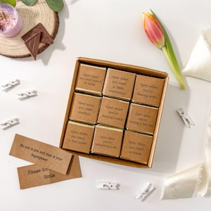 Op de afbeelding: Een doos met kleine chocolade reepjes met aanmoedigende boodschappen op elk. De boodschappen zijn: "Open wanneer je wat motivatie nodig hebt", "Open wanneer je je eenzaam voelt", en "Open wanneer je een pauze nodig hebt".