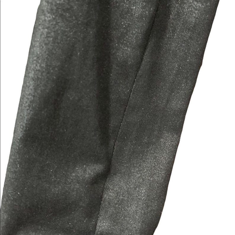 May include: Close-up of a section of black fabric with a subtle sheen. The fabric is divided by a vertical seam, creating two distinct panels. The texture appears smooth with a slight shimmer, suggesting a formal or evening wear material.