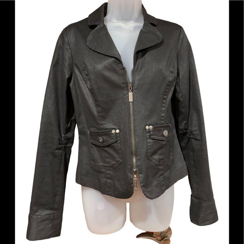 May include: A dark grey blazer with a notched collar, long sleeves, and a zip-up front. The jacket features two front pockets with button details and a tailored fit. The fabric has a subtle sheen, giving it a polished look.