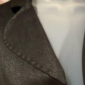 May include: Close-up of a dark brown blazer with a subtle metallic sheen. The fabric has a textured appearance, and the lapel is visible. The blazer is displayed on a white mannequin, highlighting the tailored design.