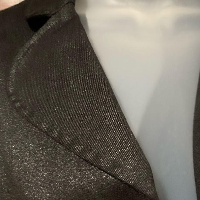 May include: Close-up of a dark brown blazer with a subtle metallic sheen. The fabric has a textured appearance, and the lapel is visible. The blazer is displayed on a white mannequin, highlighting the tailored design.