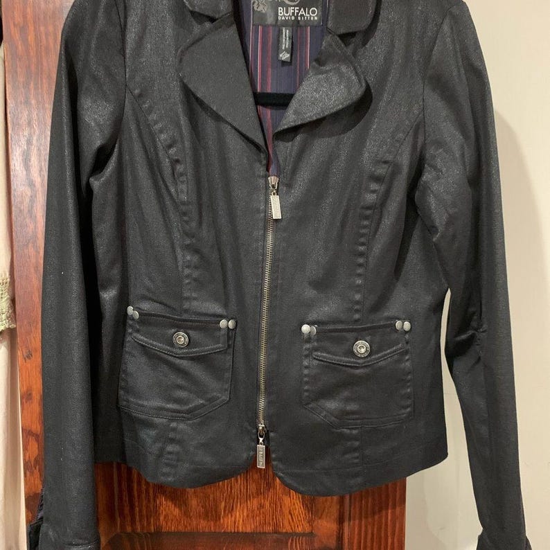 May include: A black jacket with a glossy sheen, featuring a notched collar, a full-length zip, and two front pockets with button details. The jacket has a tailored fit and the brand name "BUFFALO DAVID BITTON" is visible on the label.
