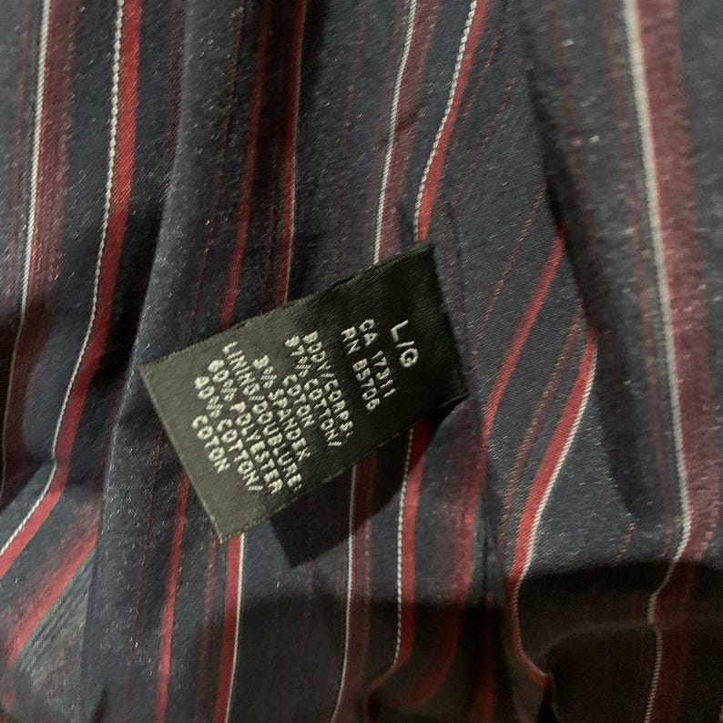 May include: A black label with white text, including "L/G", "CA 17311", and "RN 85706". The label details fabric composition: 97% cotton, 3% spandex for the body, and 60% polyester, 40% cotton for the lining. The background is a navy fabric with red and white stripes.
