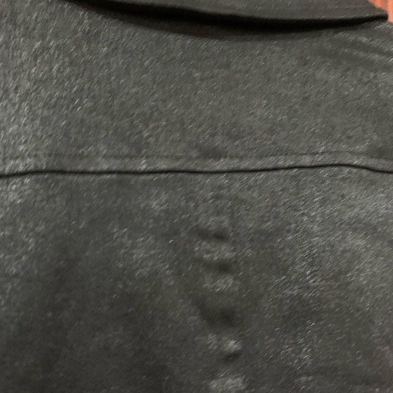 May include: Close-up of a dark grey jacket with a collar and a horizontal seam across the back. The fabric has a slightly textured appearance.