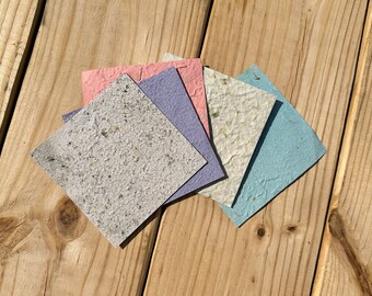 May include: Five sheets of handmade paper in various colors, including light blue, pink, purple, and white. The paper has a textured, speckled appearance and is arranged in a fan shape.