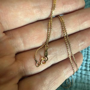 May include: A thin gold chain necklace featuring a delicate twisted rope link design. The necklace includes a circular spring ring clasp and a small metal tag clearly stamped with the text 14K, indicating the gold purity of the jewelry piece.