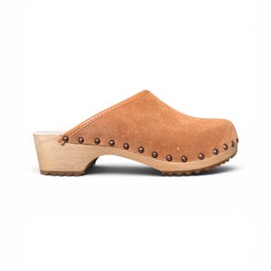 May include: A single brown suede clog with a wooden sole. The shoe has a rounded toe, a low heel, and is decorated with small, dark metal studs along the sole's edge. The interior has a light-coloured lining.
