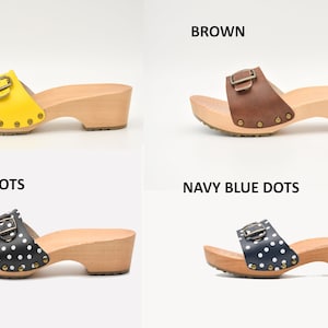 May include: Four pairs of wooden platform sandals with a buckle closure. The sandals are shown in four different colors: yellow, brown, black with white polka dots, and navy blue with white polka dots.