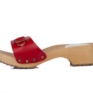 May include: Red leather clog with a buckle and a wooden heel. The clog has a studded design on the strap.
