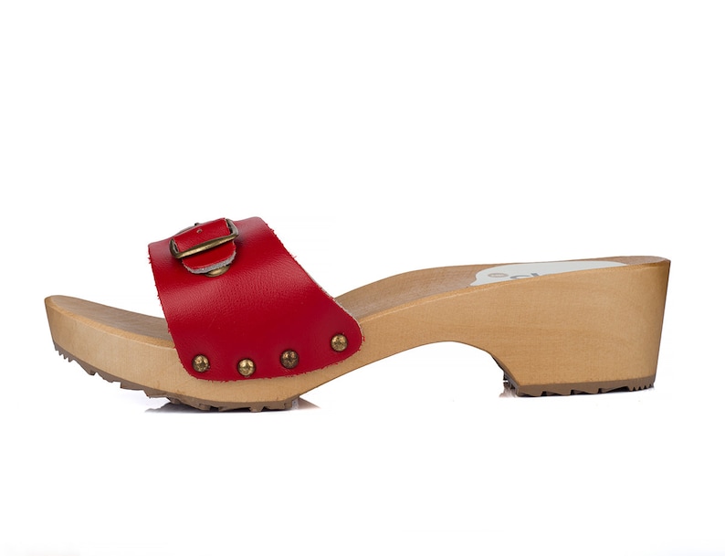 May include: Red leather clog with a buckle and a wooden heel. The clog has a studded design on the strap.