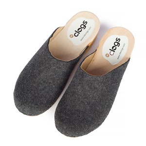 Könnte beinhalten: Paar graue Filz-Clogs mit Holzsohlen. Die Clogs haben ein Etikett auf der Oberseite, auf dem "clogs" und "www.clogs.com" steht.