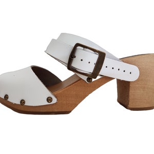 Puede incluir: Sandalias de madera con tac&oacute;n blanco de cuero, con una correa de hebilla y una suela de plataforma de madera.