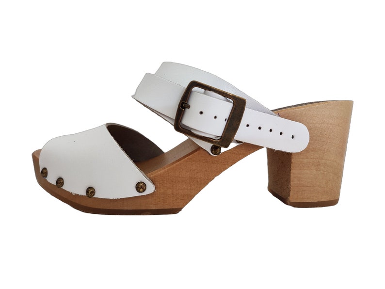 Puede incluir: Sandalias de madera con tac&oacute;n blanco de cuero, con una correa de hebilla y una suela de plataforma de madera.