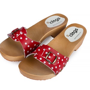 May include: A pair of red and white polka dot wooden clogs with a buckle. The clogs have a wooden heel and a leather strap.