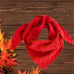 May include: A bright red triangular scarf featuring a textured knit pattern. The fabric displays a consistent woven design throughout the piece, with pointed ends and a folded structure that creates a soft, layered appearance for the accessory.
