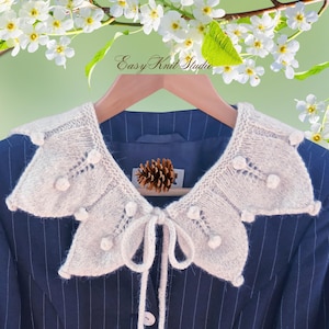May include: A cream-coloured knitted detachable collar featuring a scalloped edge with small pom-pom accents and a central tie closure. The collar is displayed on a dark blue pinstriped blazer, with the text Easy Knit Studio visible above.