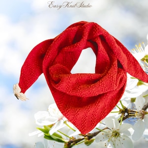May include: A vibrant red triangular scarf with a textured weave. The scarf is draped, with one end adorned with a butterfly. The background features white flowers and a soft blue sky. The text "Easy Knit Studio" is in the upper left corner.