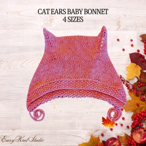 May include: A pink and orange variegated knit baby bonnet featuring two pointed cat ears at the top and two curled ties at the bottom. The text CAT EARS BABY BONNET 4 SIZES is printed above the bonnet, and Easy Knit Studio is printed below.