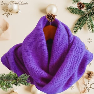 May include: A purple knitted infinity scarf. The scarf is folded in half and draped over a wooden hanger. The scarf is soft and cozy and would be perfect for keeping warm in the winter.