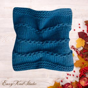May include: A square-shaped teal blue knit pillow cover featuring a textured pattern of horizontal ridges and alternating rows of stockinette and garter stitches. The fabric has a soft, yarn-based appearance with a consistent deep blue color.